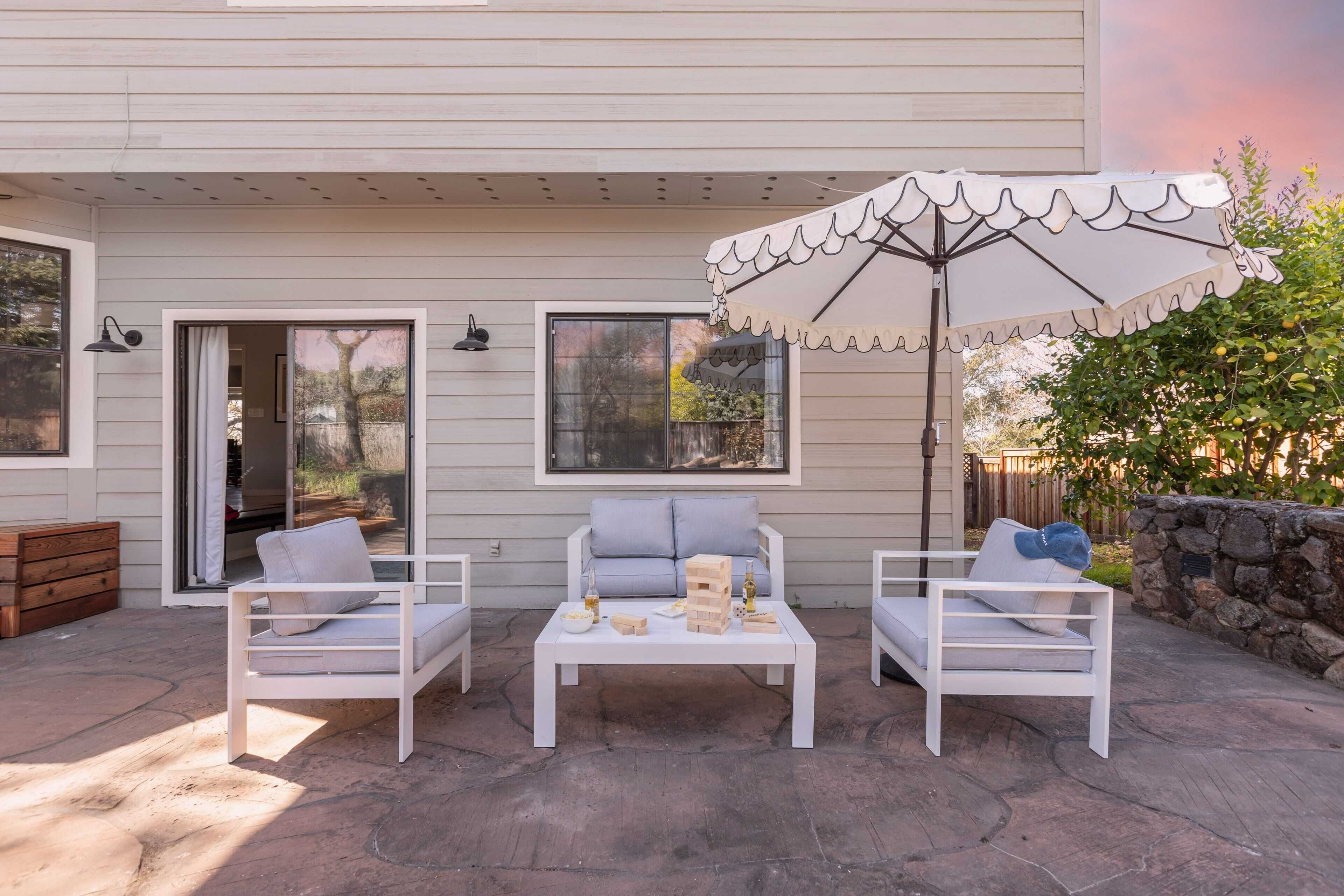 Une terrasse extérieure avec des meubles blancs, notamment deux chaises et une table, ainsi qu’un parasol décoratif.