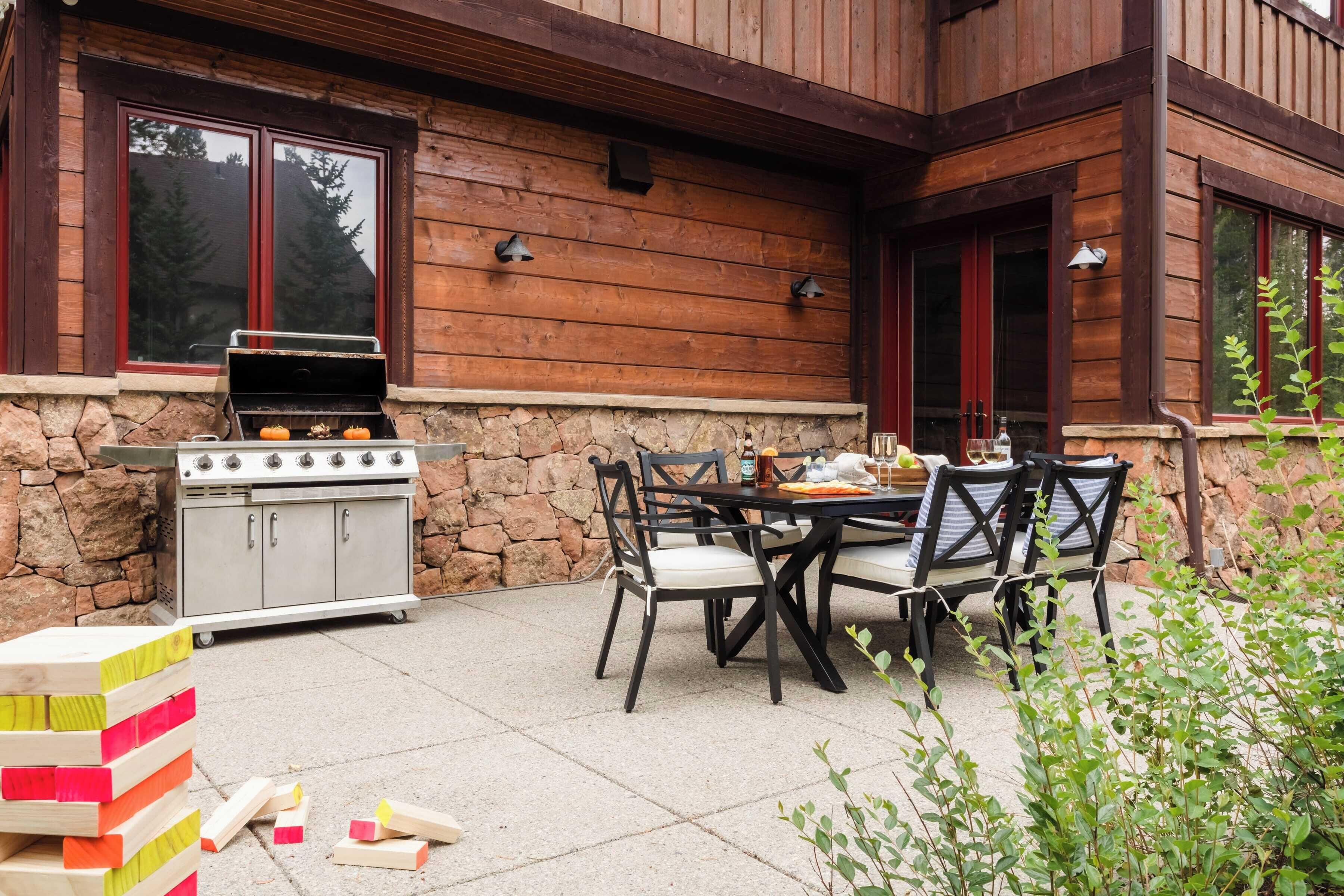 An outdoor patio with a stone wall, wooden deck, and a grill.