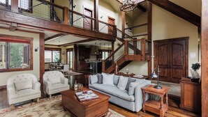 A spacious living area with a high ceiling, wooden staircase, and a dining area with a view.