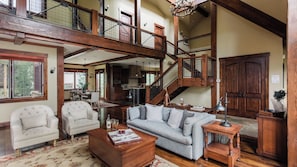 A spacious living area with a high ceiling, wooden staircase, and a dining area with a view.