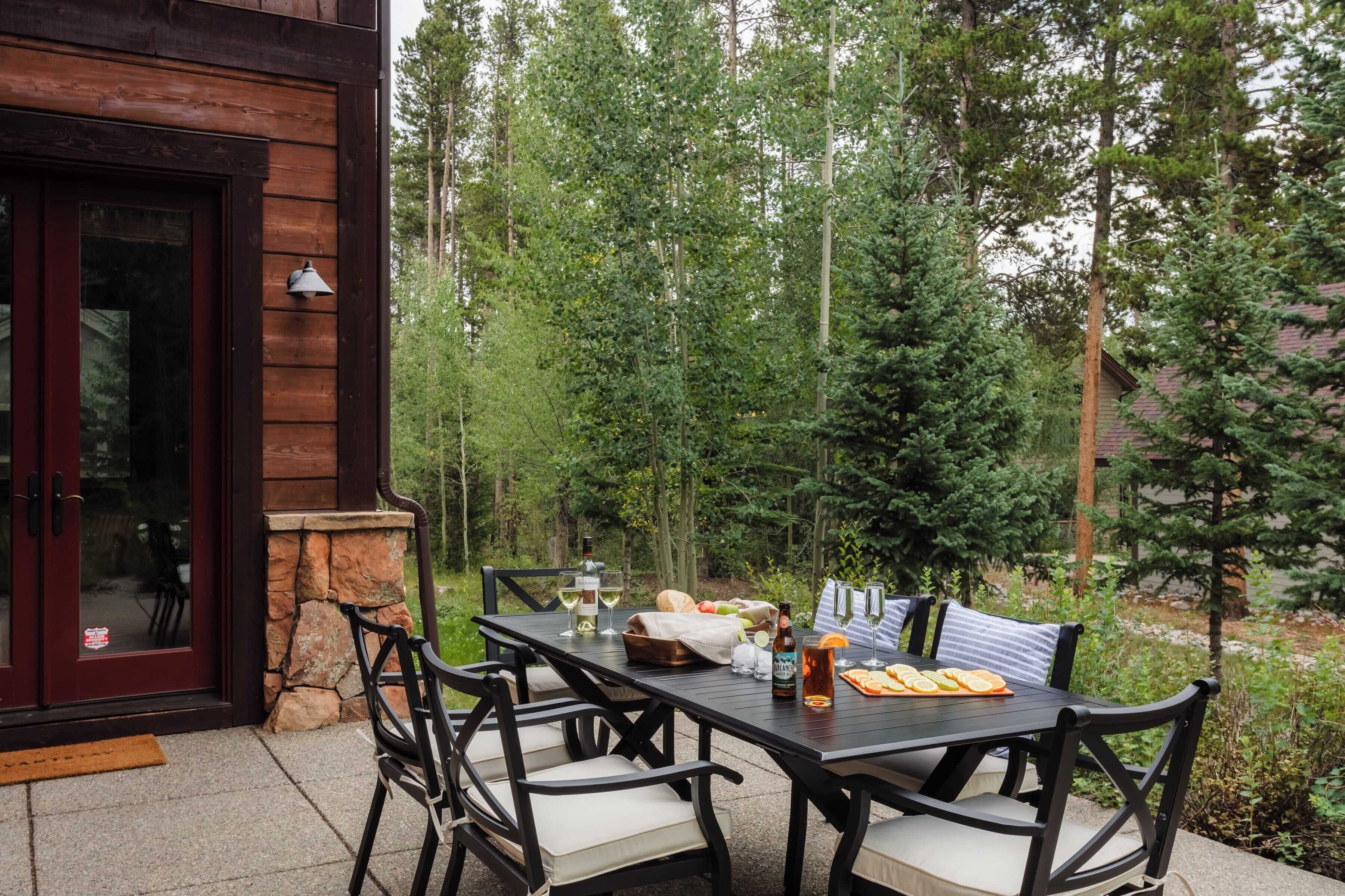 Un espace extérieur aménagé pour les repas, avec une table et des chaises en bois, entouré d’arbres.