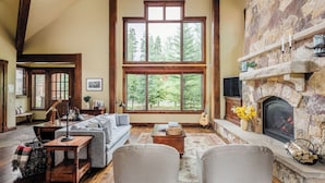 A cozy living room with a fireplace, large windows, and a stone wall.