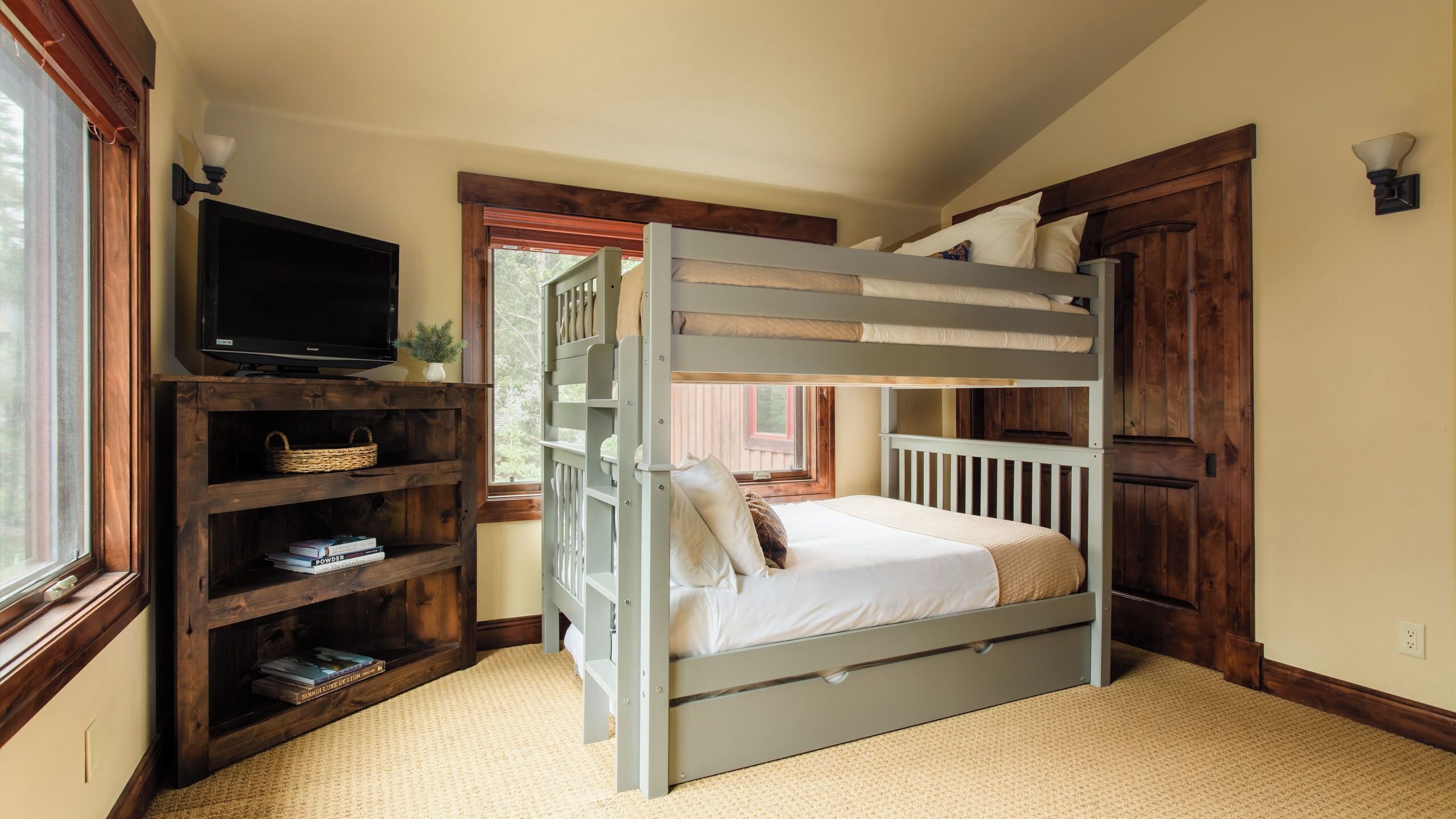 A bunk bed with a television on a wooden shelf, a window, and a door.