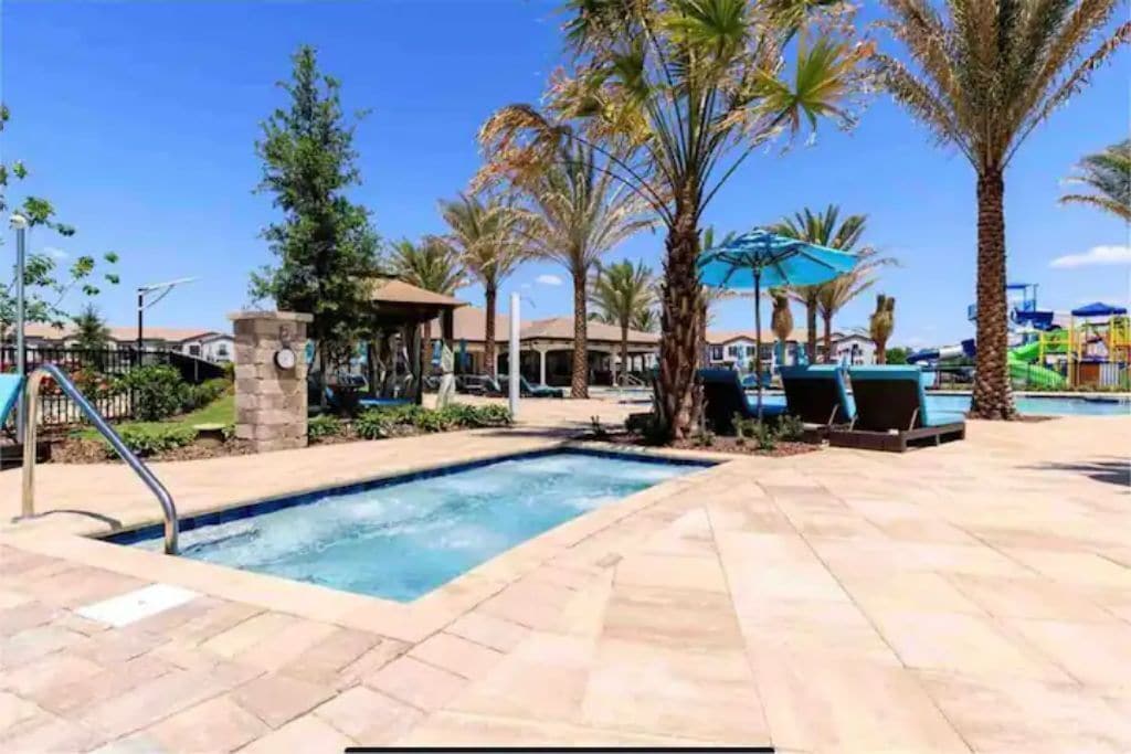 A swimming pool area with palm trees, lounge chairs, and a clear blue sky.