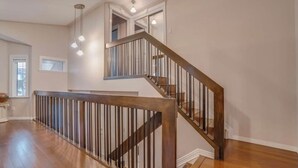 A spacious room with hardwood flooring, a wooden staircase with metal railings, and a large window providing natural light. - Big family home w/ Deck, Ping Pong, BBQ & Garage (Edmonton)