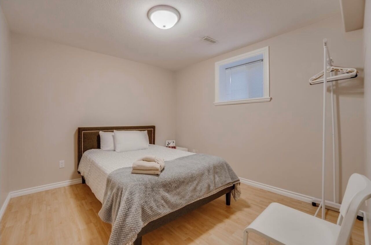 A bedroom with a bed, a chair, a hanging clothes rack, and a window.