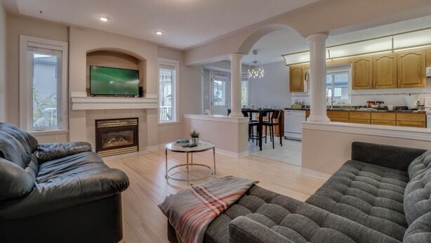 A spacious living room with a fireplace, a television, and a dining area with a kitchen in the background. - Big family home w/ Deck, Ping Pong, BBQ & Garage (Edmonton)