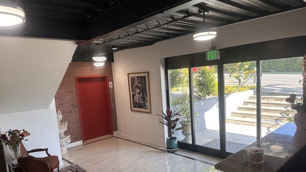 A lobby with a red door, a framed picture, a potted plant, a patterned rug, and a marble floor. - Lakeview Hotel (Kirkland)