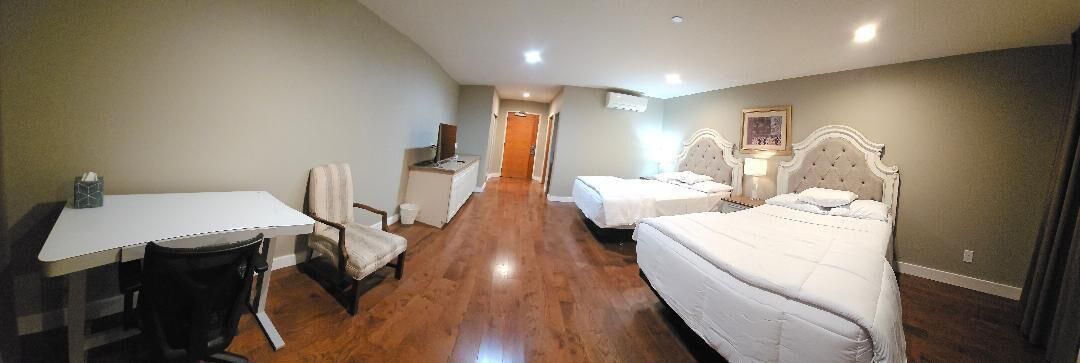 A hotel room with a desk, two beds, a chair, and a small table.