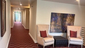 A hotel lobby with a red patterned carpet, two armchairs with red cushions, a black ottoman, and a large abstract painting on the wall. - Lakeview Hotel (Kirkland)