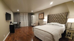 A hotel room with a large bed, a flat-screen TV mounted on the wall, a desk with a chair, and a wardrobe. - Lakeview Hotel (Kirkland)