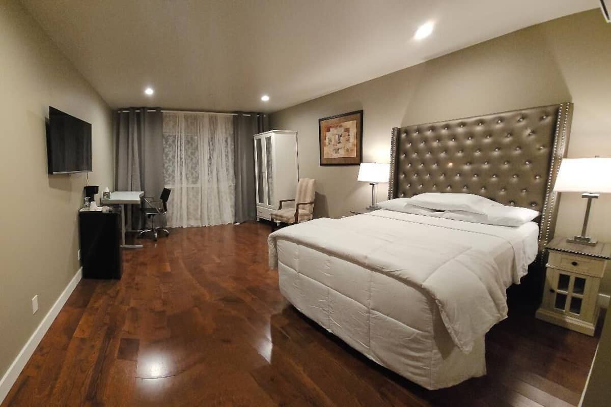 A hotel room with a large bed, a flat-screen TV mounted on the wall, a desk with a chair, and a wardrobe.