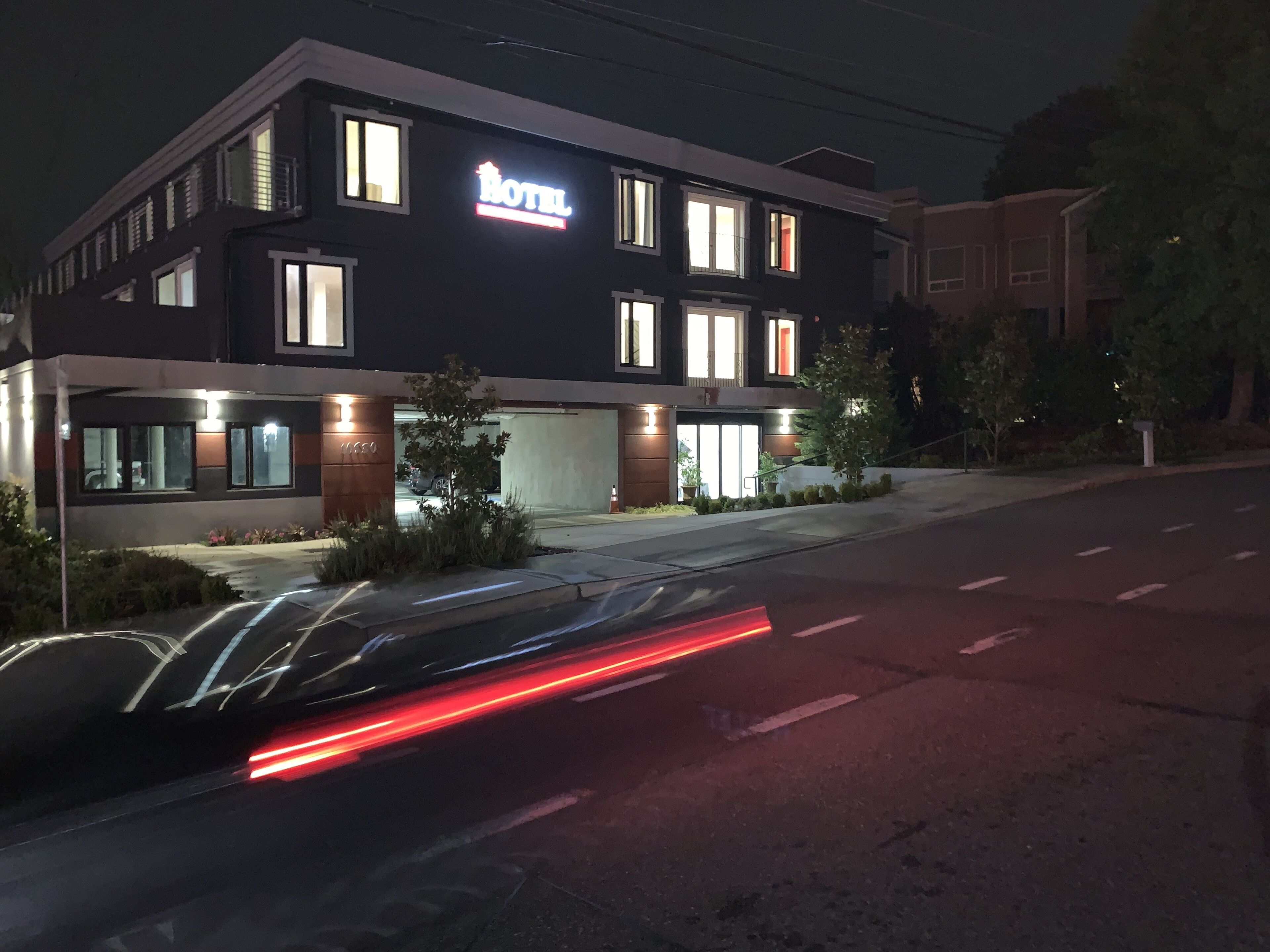 Un hotel moderno con un llamativo letrero 'HOTEL', un área de estacionamiento techada y una fachada bien iluminada.
