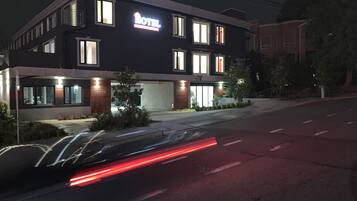 Un hotel moderno con un llamativo letrero 'HOTEL', un área de estacionamiento techada y una fachada bien iluminada.