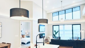 Una cocina moderna con una isla central, luces colgantes y un amplio ventanal con vistas a un paisaje urbano.