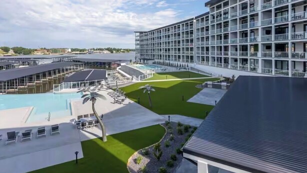 Un hotel moderno con zona de piscina, varios balcones y vista al puerto deportivo.