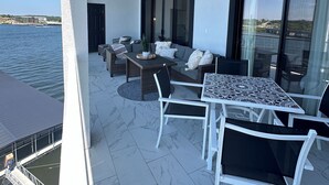 Un balcón moderno al aire libre con zona de comedor, asientos y vista al agua.