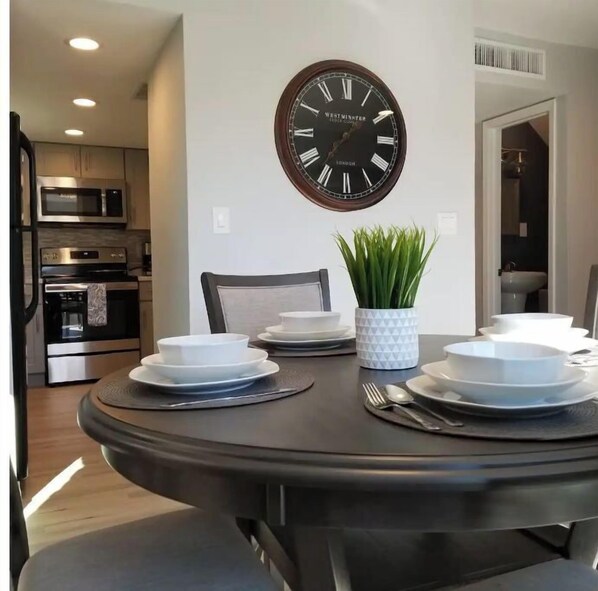 Enjoy meals in this dining area with a round table for four, featuring a centerpiece of green foliage and a wall-mounted clock.