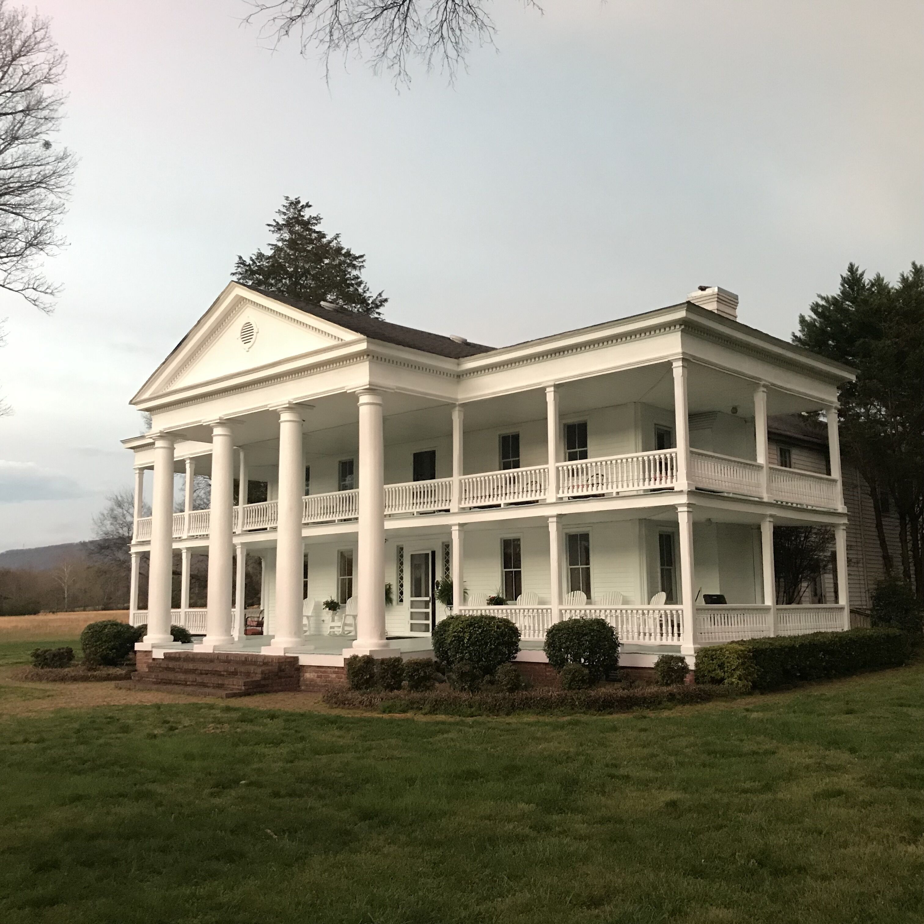 A two-story colonial-style building with a central portico, multiple balconies, and a well-maintained lawn.
