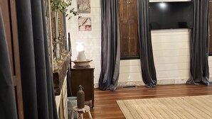 Una habitación acogedora con vigas de madera, un ventanal con cortinas, una pequeña mesa y una alfombra.