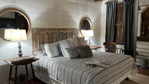 Un dormitorio con una cama grande, dos mesitas de noche con lámparas, un cabecero de madera y un espejo sobre la cama.