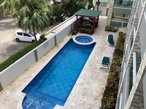 A rectangular swimming pool with a small hot tub, surrounded by a low wall and a palm tree. There are lounge chairs and a covered seating area nearby. - Beachfront Jr Penthouse *Amazing Views*1 min walk to Beach/Restaurants Elevator (Sosúa)