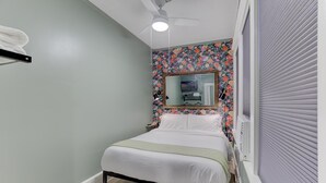 A bedroom with a bed, a ceiling fan, a mirror, and a window with blinds. - Tiny Trendy Traveler's Studio in Historic Midtown! (Memphis)