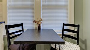 A dining table with two chairs, a vase with dried flowers, and a window with blinds. - Tiny Trendy Traveler's Studio in Historic Midtown! (Memphis)