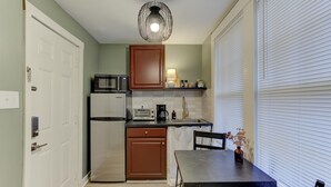 A compact kitchen with a microwave, toaster, and refrigerator. There is a dining table with chairs and a window with blinds. - Tiny Trendy Traveler's Studio in Historic Midtown! (Memphis)