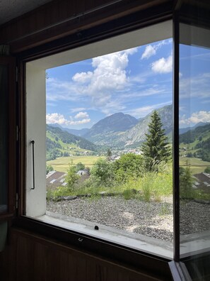 Une fenêtre donnant sur un paysage montagneux, avec des champs verdoyants et un ciel dégagé.