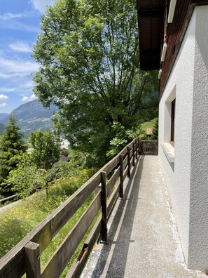 Un balcon offrant une vue sur un paysage montagneux, avec une balustrade en bois et un bâtiment à la façade blanche.