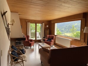 Un salon chaleureux avec des boiseries, une grande fenêtre offrant une vue panoramique et des sièges confortables.