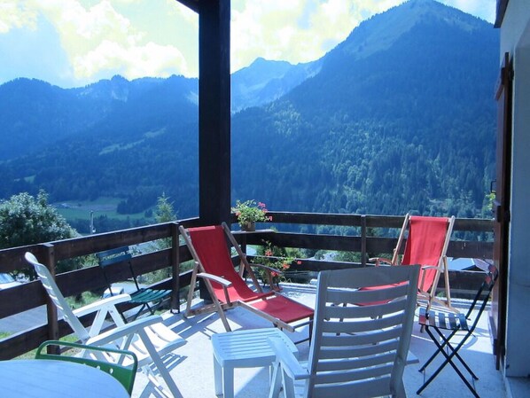 Un balcon avec vue sur les montagnes, comprenant plusieurs chaises et une table.