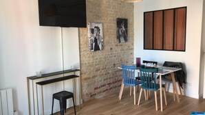 A modern kitchen with a brick wall, a dining table with chairs, and a TV mounted on the wall.