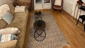 A living room with a brown sofa, a patterned rug, a small round table, and a brick wall.