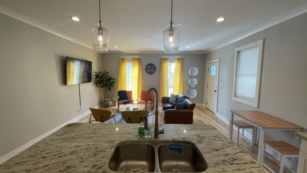 A kitchen with a granite countertop, stainless steel sink, and pendant lighting. There is a dining area with a table and chairs, and a living room with a sofa and a coffee table. - Bright, Cheery Home steps from Shops & Nightlife! (Louisville)