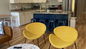 A modern kitchen with white cabinets, stainless steel appliances, and a blue island with bar stools. - Bright, Cheery Home steps from Shops & Nightlife! (Louisville)