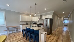 A modern kitchen with a central island, bar stools, stainless steel appliances, and a wooden floor. - Bright, Cheery Home steps from Shops & Nightlife! (Louisville)