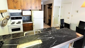 A kitchen with wooden cabinets, a white refrigerator, a stove, and a marble countertop.