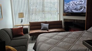 A hotel room with a large bed, a sofa, a television, and a fireplace.