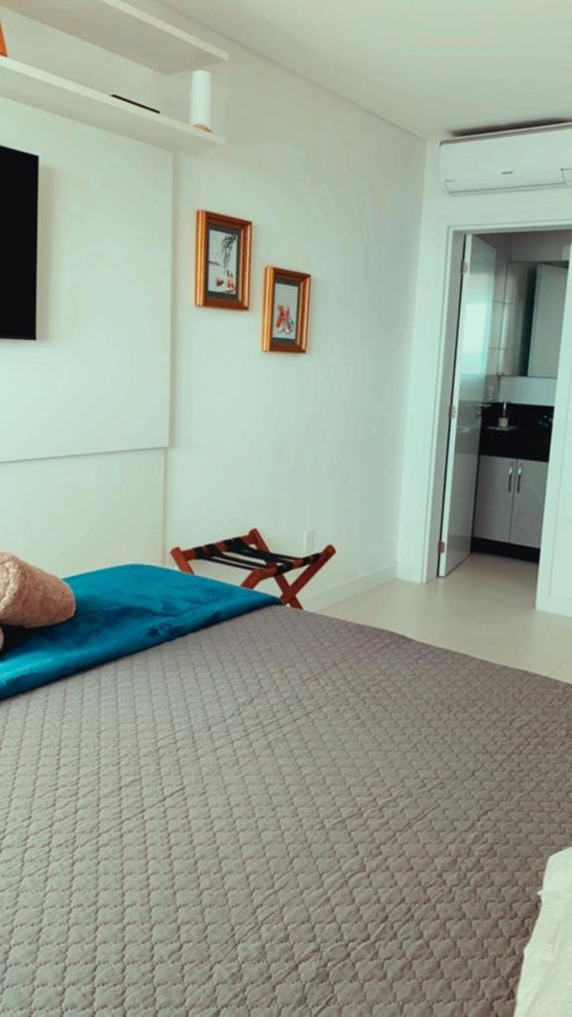 Ein Schlafzimmer mit einem Bett, einem Sessel, einem an der Wand befestigten Fernseher und einer Tür zu einer Küche.