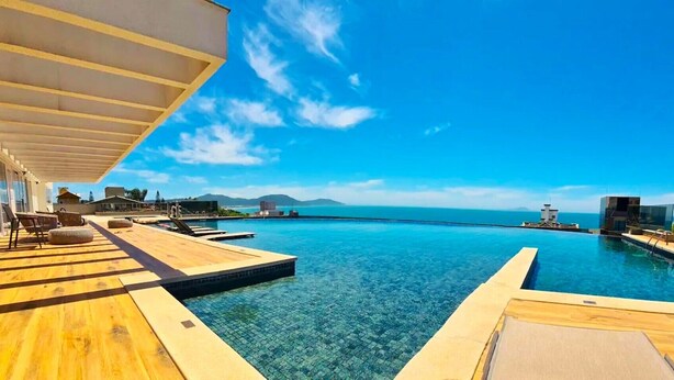 Un espace aménagé au bord de la piscine, avec une terrasse en bois, des chaises longues et une vue dégagée sur l’océan.