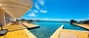 Ein Poolbereich mit Holzterrasse, Liegestühlen und freiem Blick auf den Ozean.
