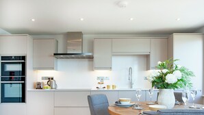 Una cocina moderna con electrodomésticos integrados, un comedor con una mesa redonda y sillas, y un jarrón con flores sobre la mesa.