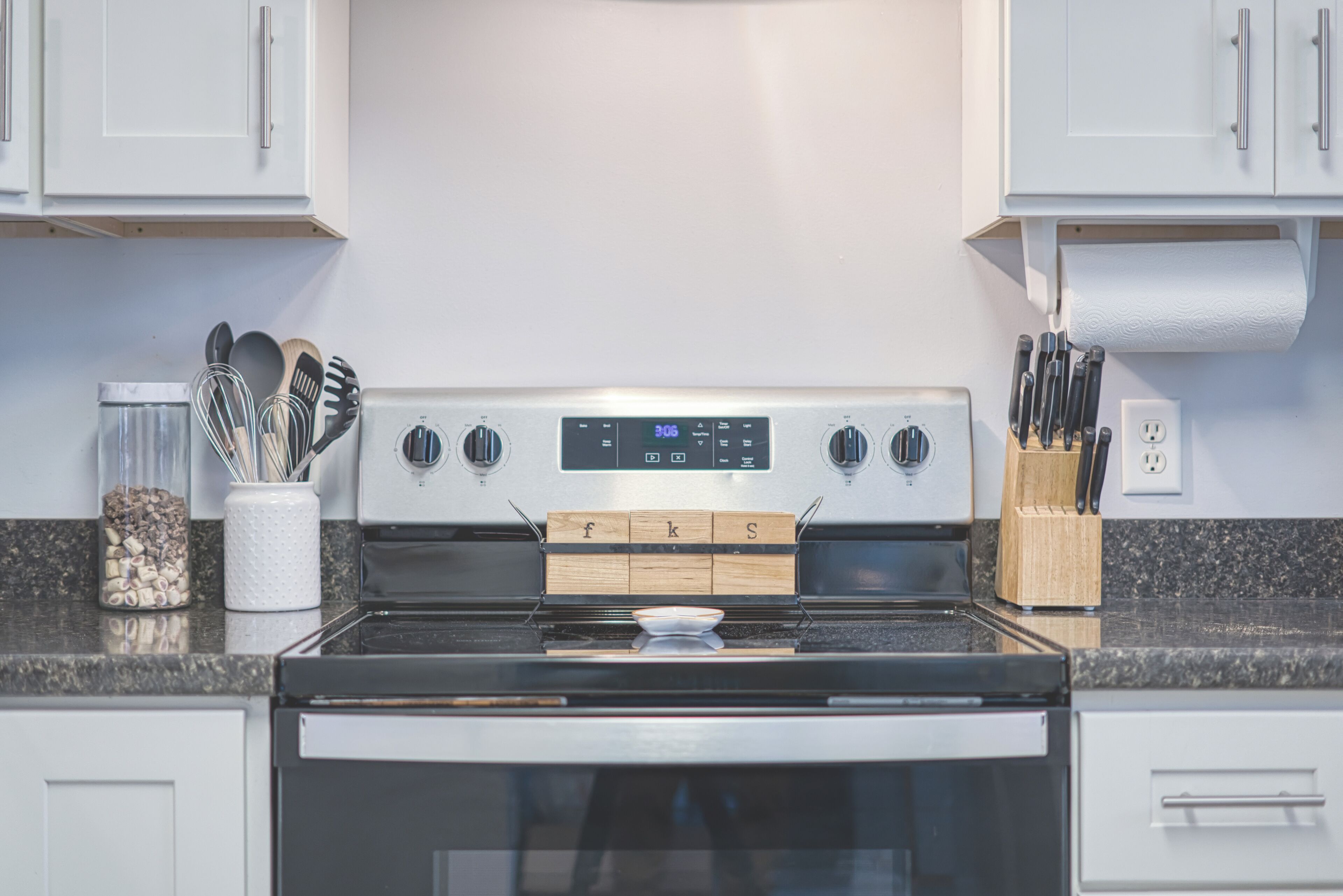 A modern kitchen with white cabinets, a stainless steel stove, and a granite countertop.