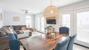 Een moderne woonkamer met een houten eettafel, blauwe fauteuils, een grijze bank en een geweven hanglamp.