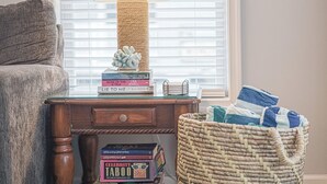 Een houten nachtkastje met een lamp, een stapel boeken en een gevlochten mand met handdoeken.