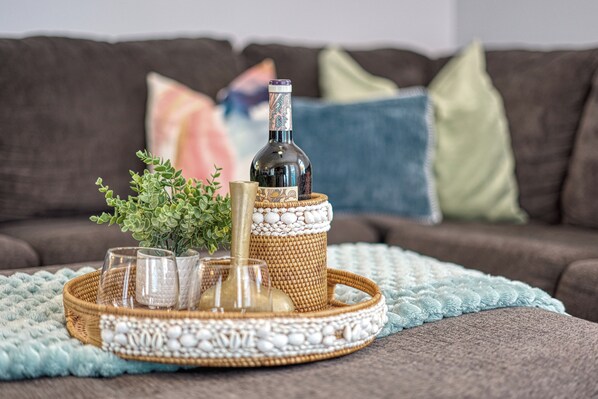 A wicker tray with a bottle, glasses, and a plant on a couch.