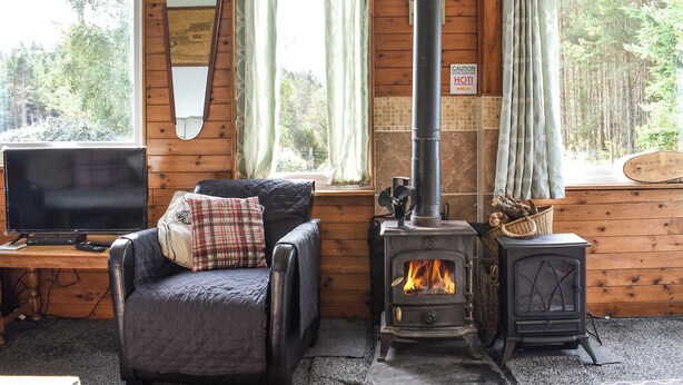 A cozy cabin interior with a wooden interior, a fireplace, a television, and a comfortable chair.