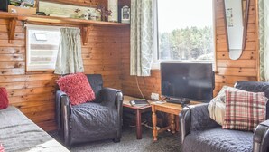 A cozy cabin interior with wooden walls, a large window, a television, and two leather chairs.